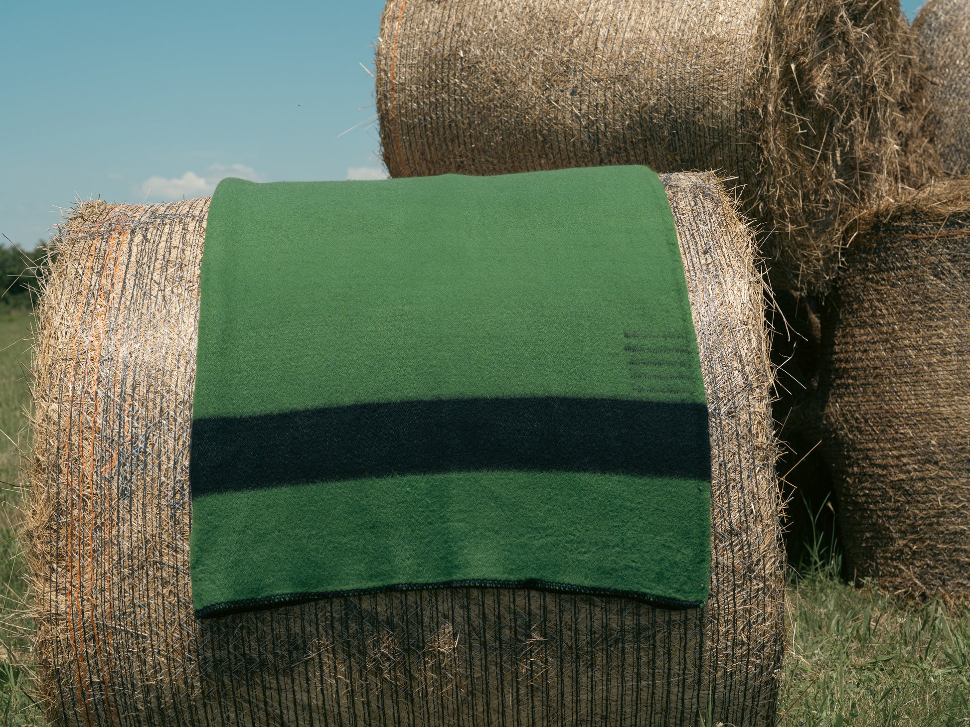 Hay bale with a top quality green striped blanket on top in an outdoor setting