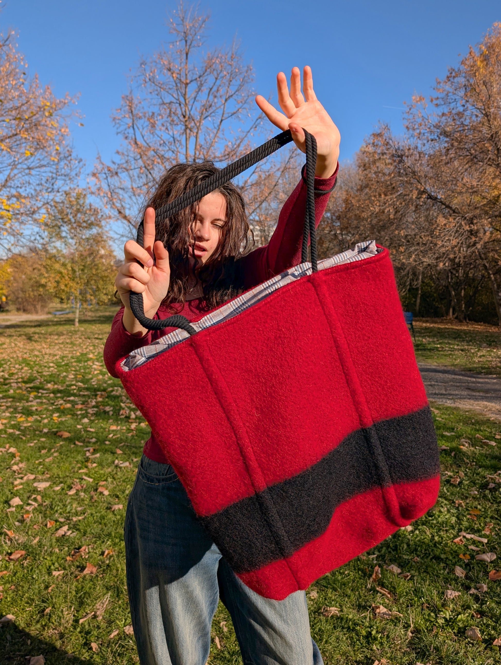 A young woman showing a large stylish red shopper bag with black robe straps and a stylish black stripe, upcycled from pure wool blanket.