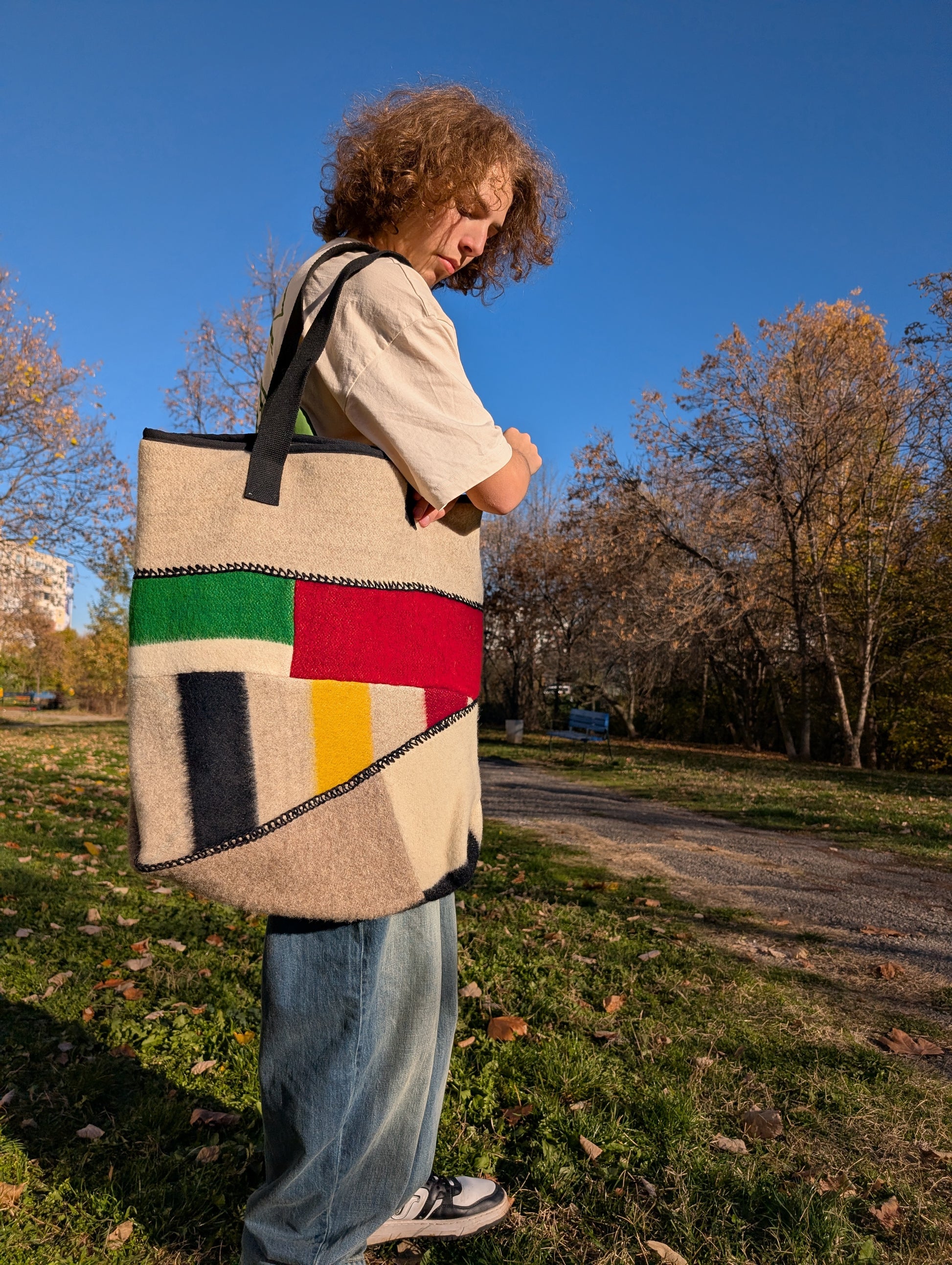 Young man in T-shirt and jeans wearing a large shopping bag with colorful patcwhork front, upcycled from various wool blanket cuts.