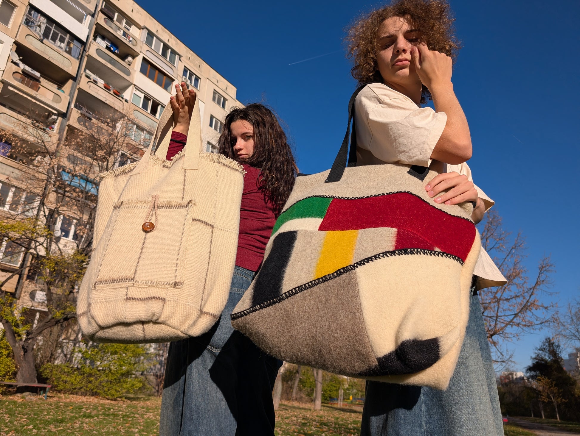Two persons, each holding a modern made-to-order handmade tote bag or shopping bag upcycled from natural sustainable wool blanket cuts.
