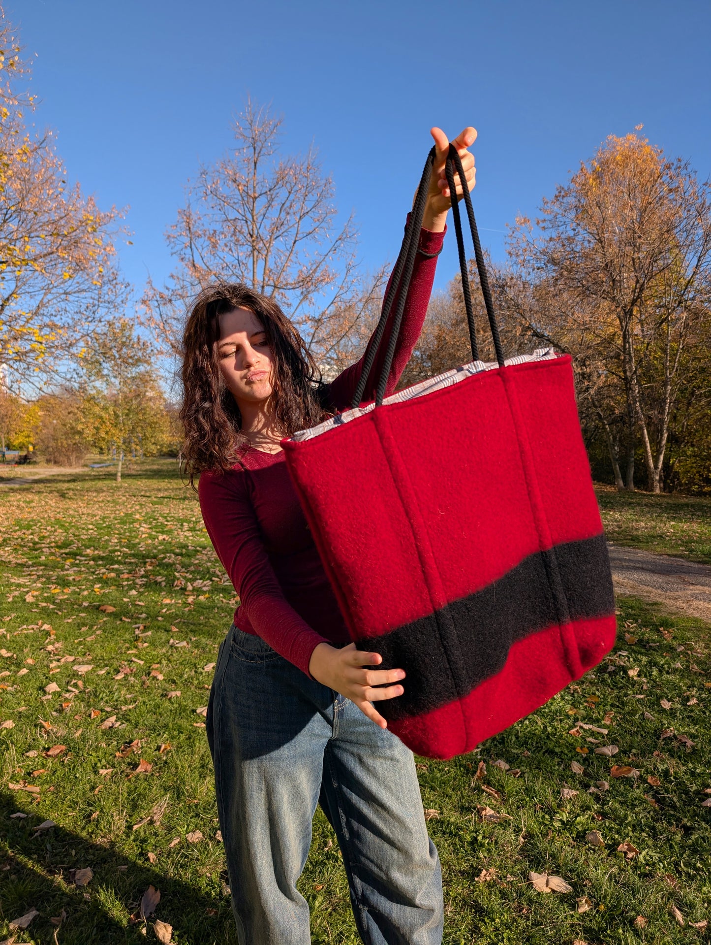 Young woman showing a large modern statement tote bag in red with a vertical black stripe and black rope handles. Bespoke shopper made from luxurious wool blanket.