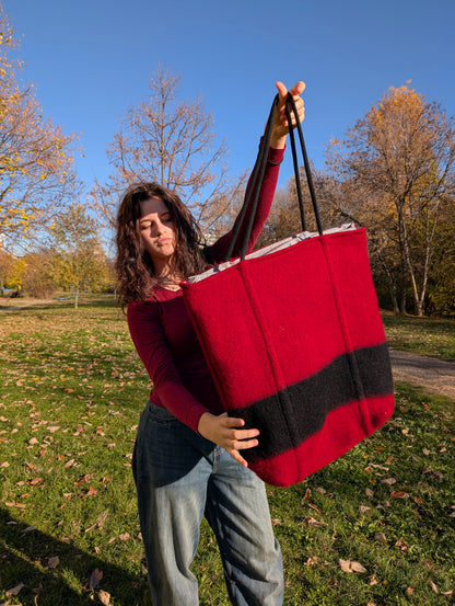 Young woman showing a large modern statement tote bag in red with a vertical black stripe and black rope handles. Bespoke shopper made from luxurious wool blanket.