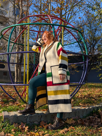 A woman leaning on a jungle gym and wearing a cardigan coat with ivory base and milti stripe pattern.