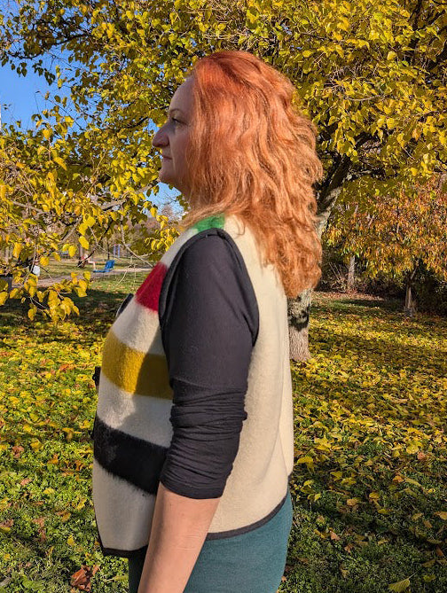 Woman wearing a cropped bespoke vest in beige or ivory base, with colorful stripes at the front and toggle closure, suitable for  rendezvous, walks, street- and everyday wear.