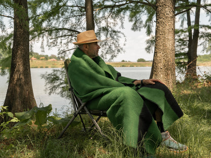 Man wrapped in a thick green wool blanket while sitting outdoors.