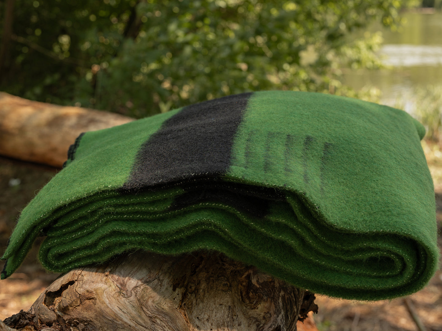 Folded green woolen blanket on a tree stump with a natural background. Local handcrafted heirloom piece.  Native traditional blanket.