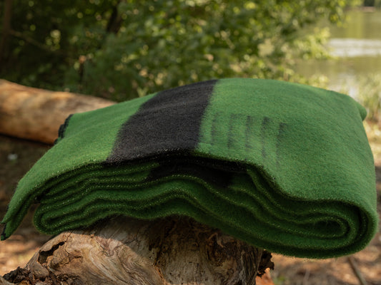 Folded green woolen blanket on a tree stump with a natural background. Local handcrafted heirloom piece.  Native traditional blanket.