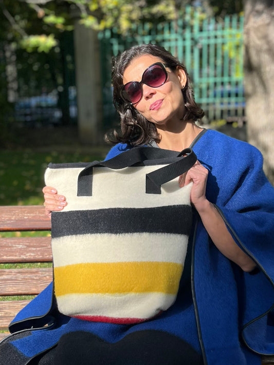 Woman holding an upcycled wool blanket tote bag with wide colorful stripes in black, yellow and red at the bottom.