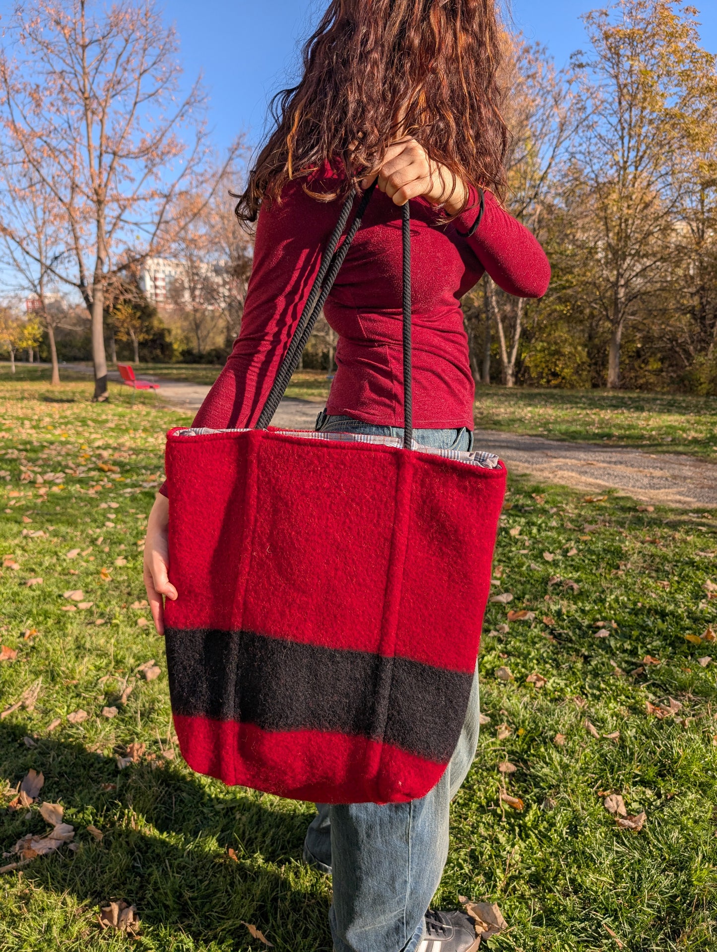 Young woman holding a large unisex functional red wool bag for shopping, walks and errands. Bespoke slow fashion artesan product with unique characteristics.