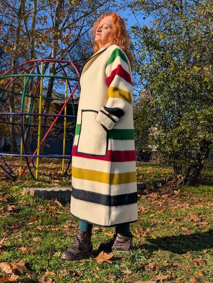 A woman wearing a loose long upcycled robe coat with shawl collar. The woman is leaning on a Jungle gym out in the park