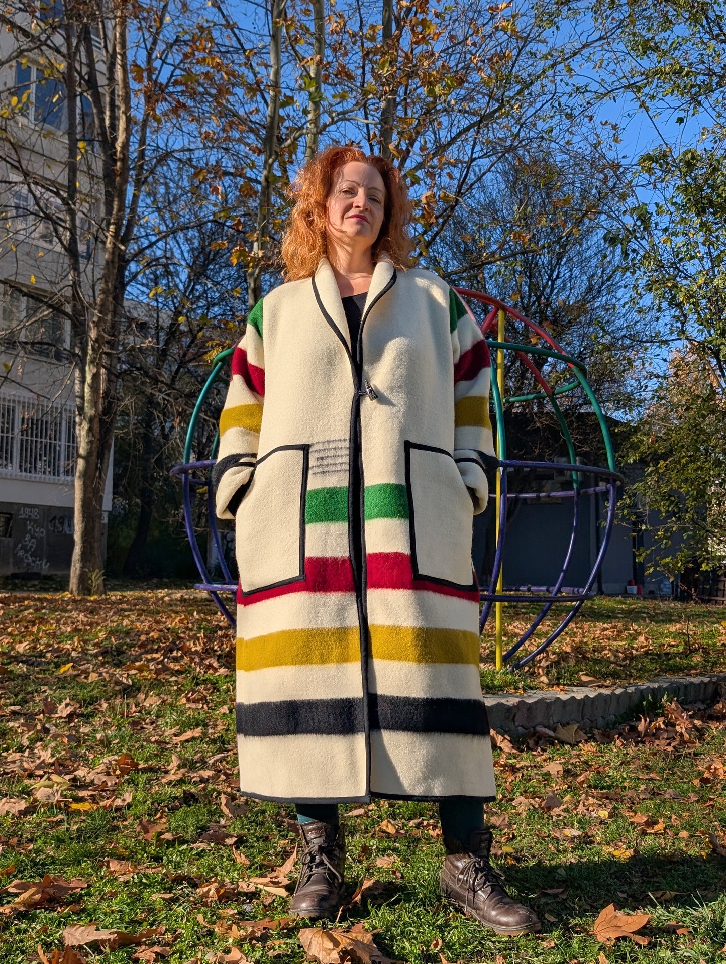 A woman posing with an oversized handmade jacket with various wide stripes, upcycled from a pure wool   blanket 