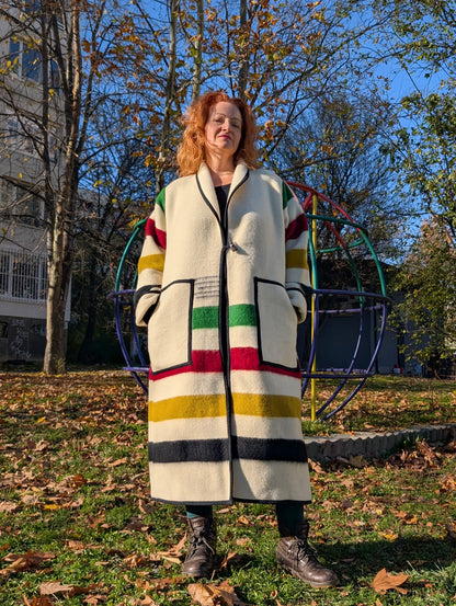 A woman posing with an oversized handmade jacket with various wide stripes, upcycled from a pure wool   blanket 