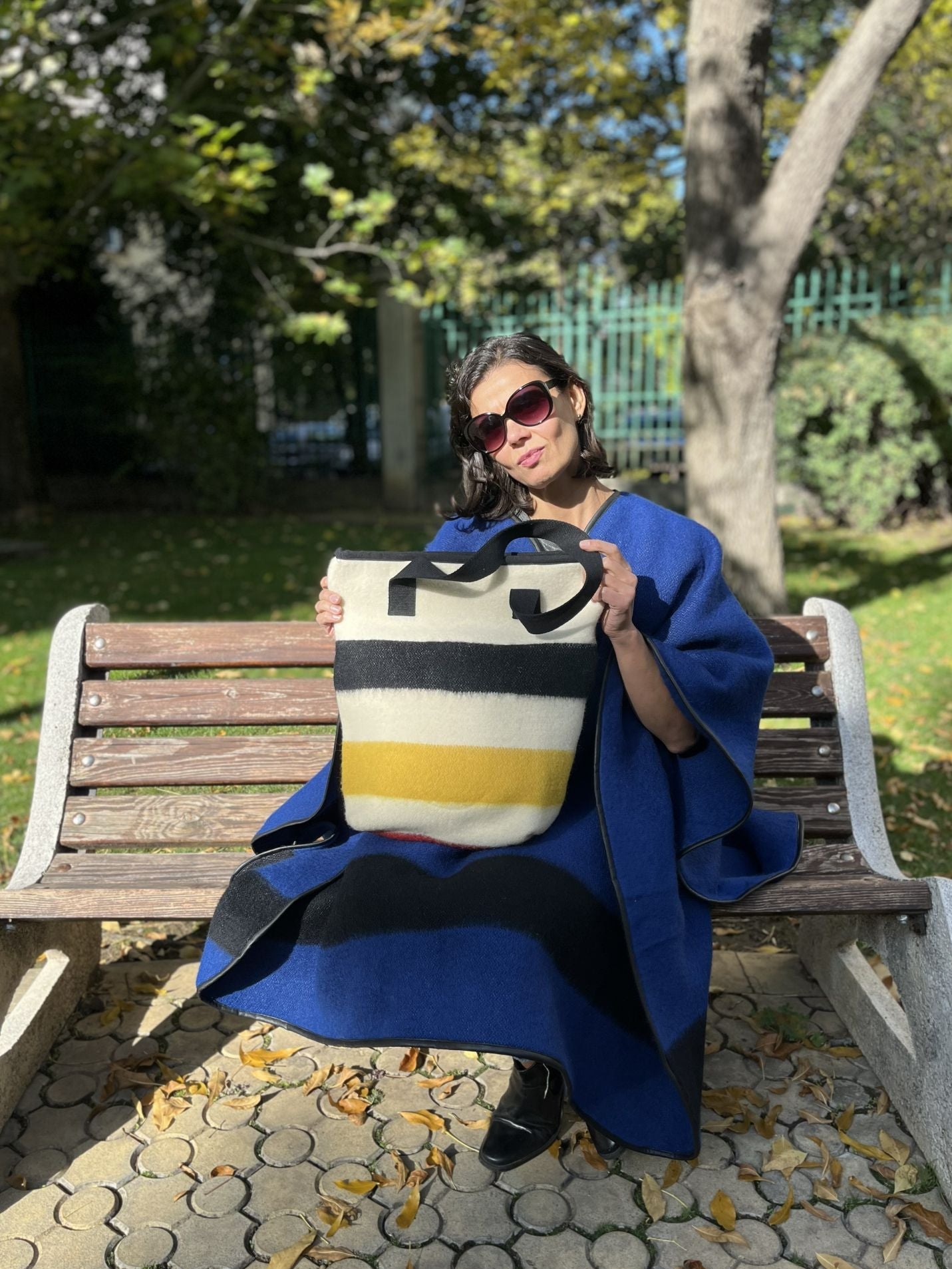 Woman sitting on a bench with a fashionable colorful bag, made from traditional wool blanket cuts.