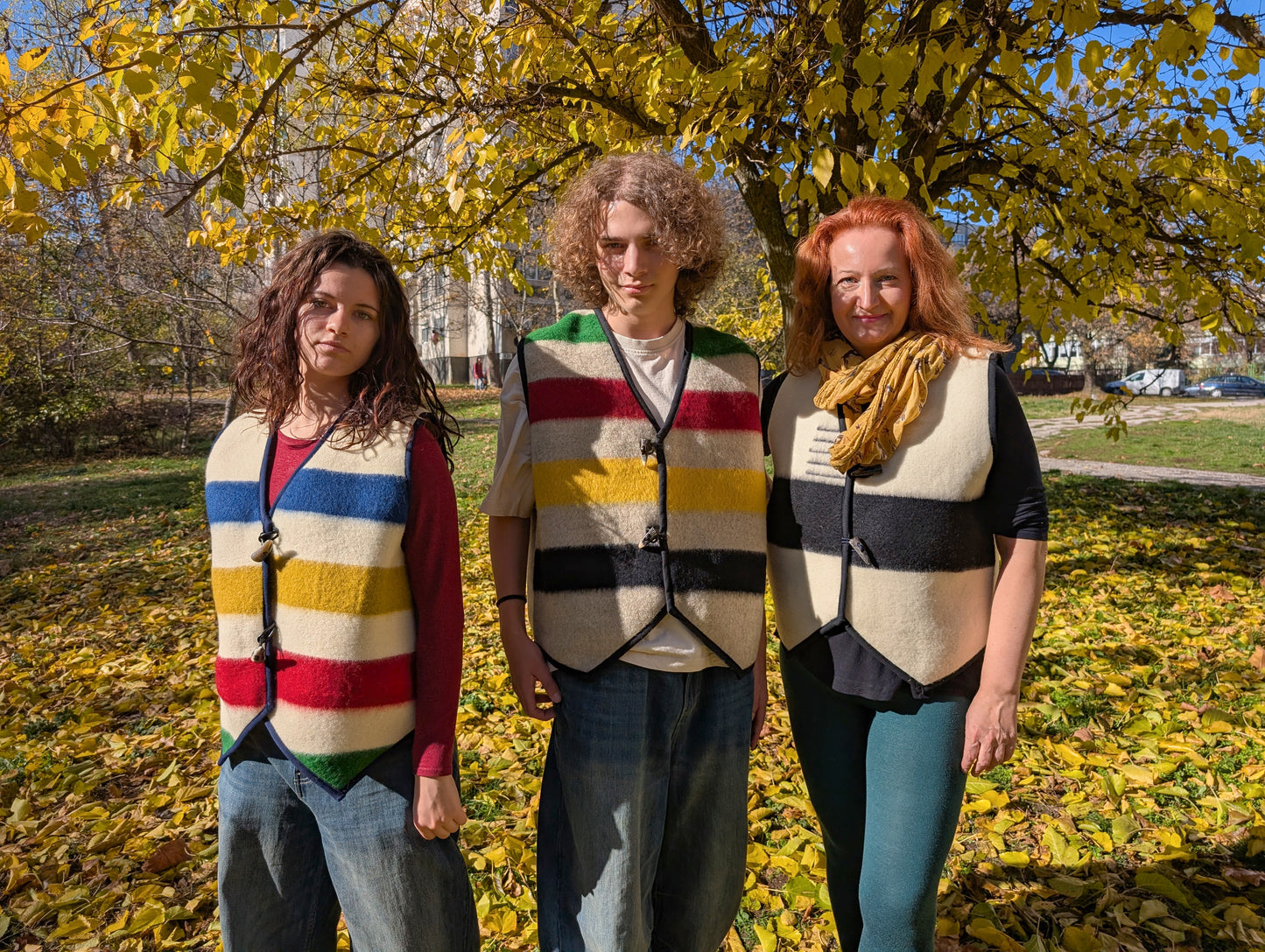 Three people wearing different models of upcycled blanket vests with multiclored stripes and toggle closure. Bespoke unisex vests suitable for all ages and ocessions.