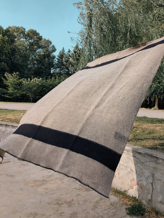 A gray wool blanket with black stripes draped in the air with trees in the background