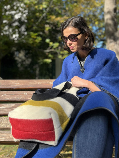 Woman sitting on a bench with a multistriped tote bag and blue coat in an outdoor setting