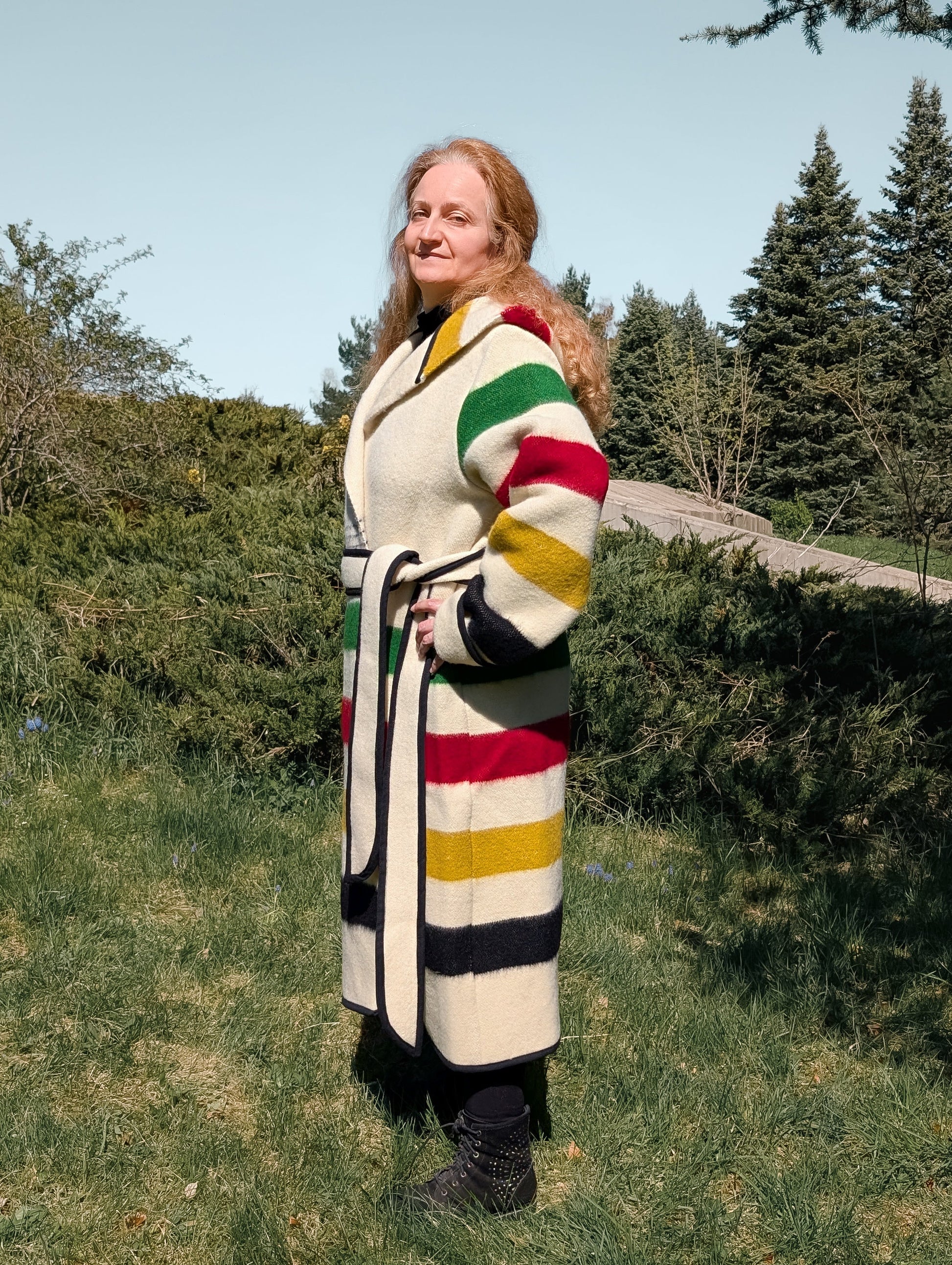 Person wearing a colorful striped coat standing outdoors with trees and grass in the background