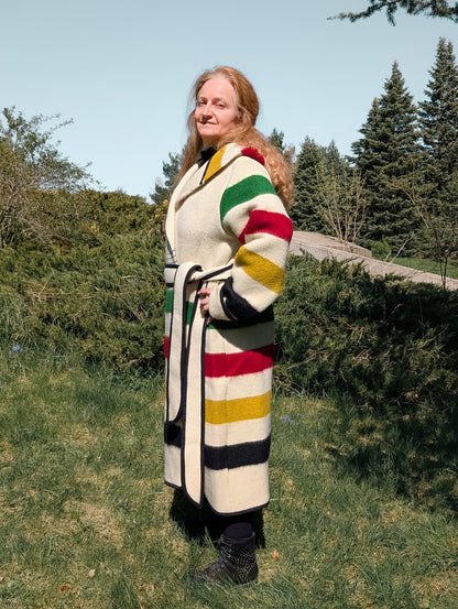 Person wearing a colorful striped coat standing outdoors with trees and grass in the background