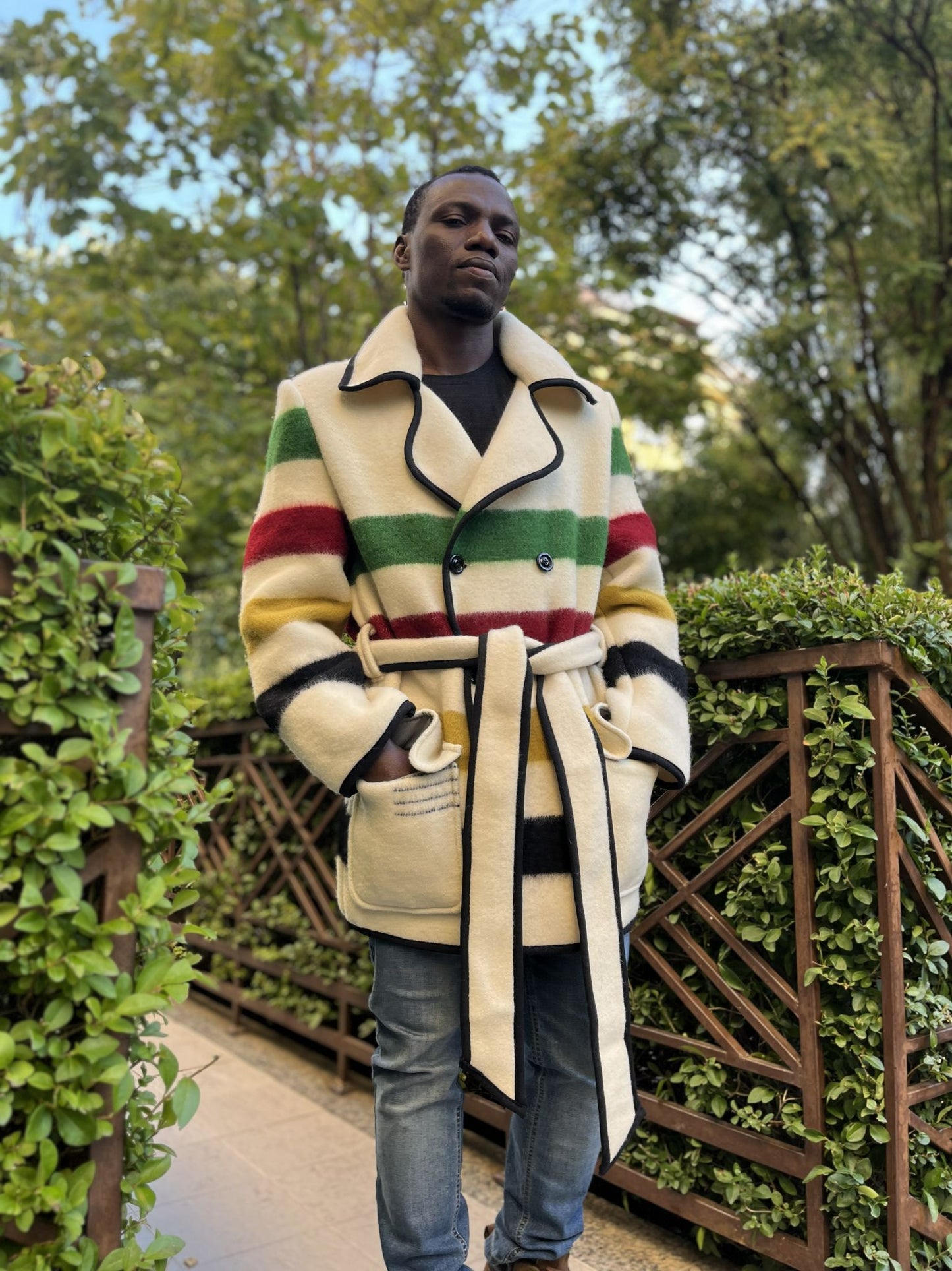 Person wearing a 1960s blanket jacket with colorful stripes, with double breasted button closure and wrapped with a belt.