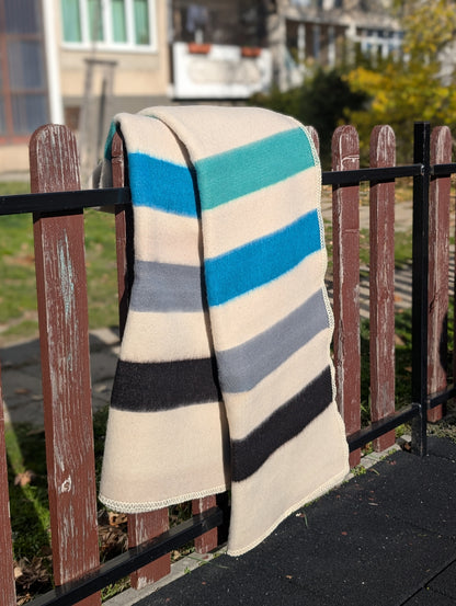 Striped pure wool blanket with blue, gray, and black stripes draped over a railing outdoors.