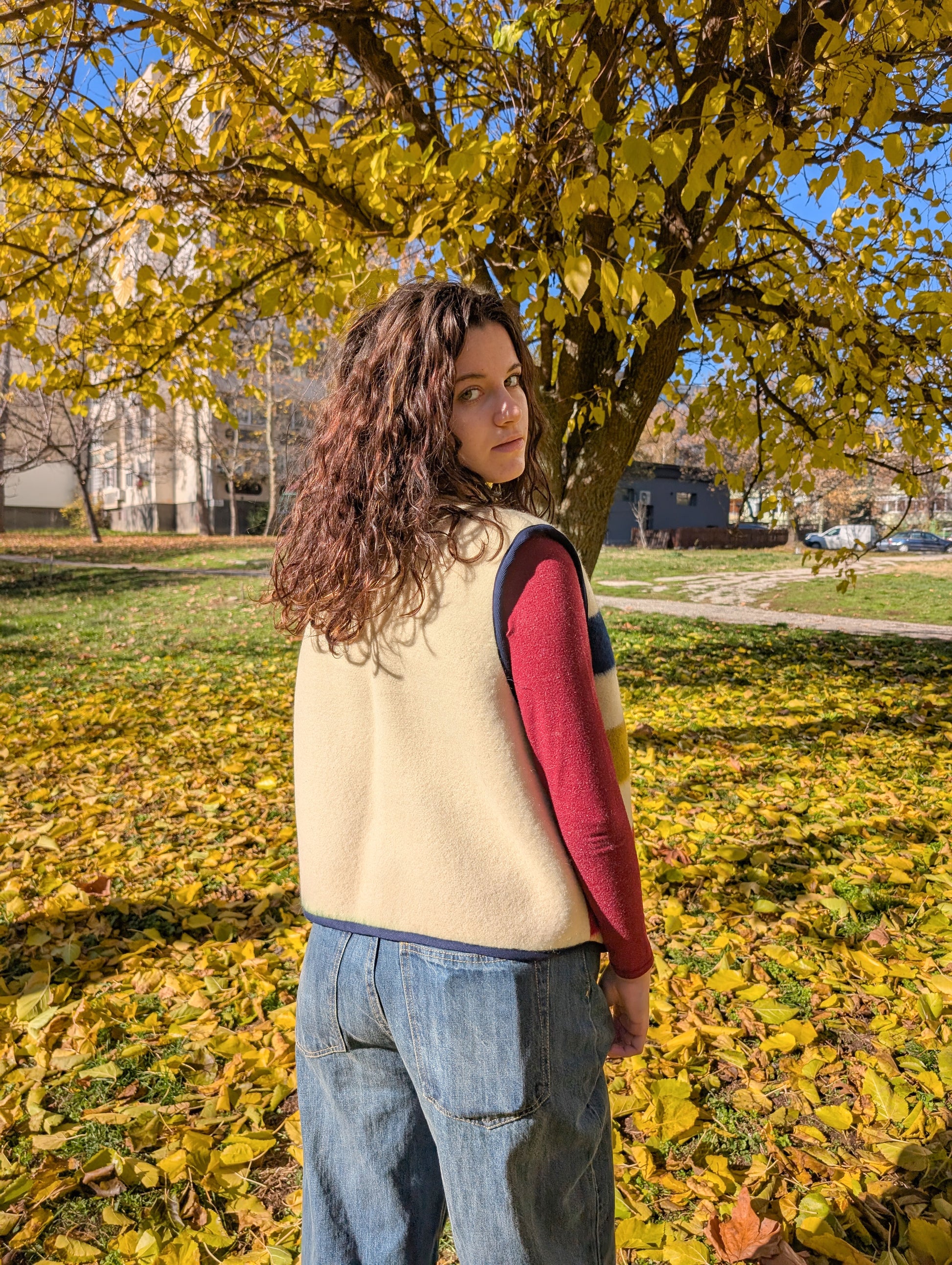 A girl standing with her back and showing the backside of a woolen vest which is plain, while the fron is with colorful stripes. The vest is made of a woolen blanket,