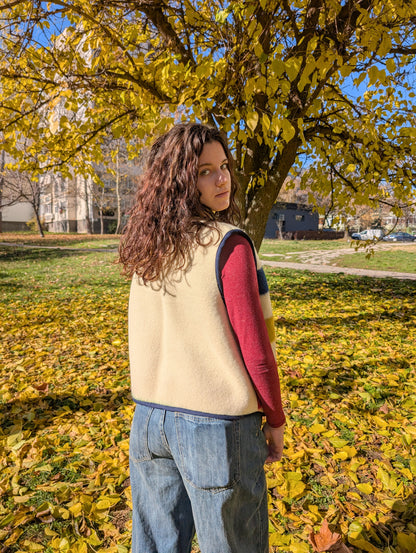 A girl standing with her back and showing the backside of a woolen vest which is plain, while the fron is with colorful stripes. The vest is made of a woolen blanket,