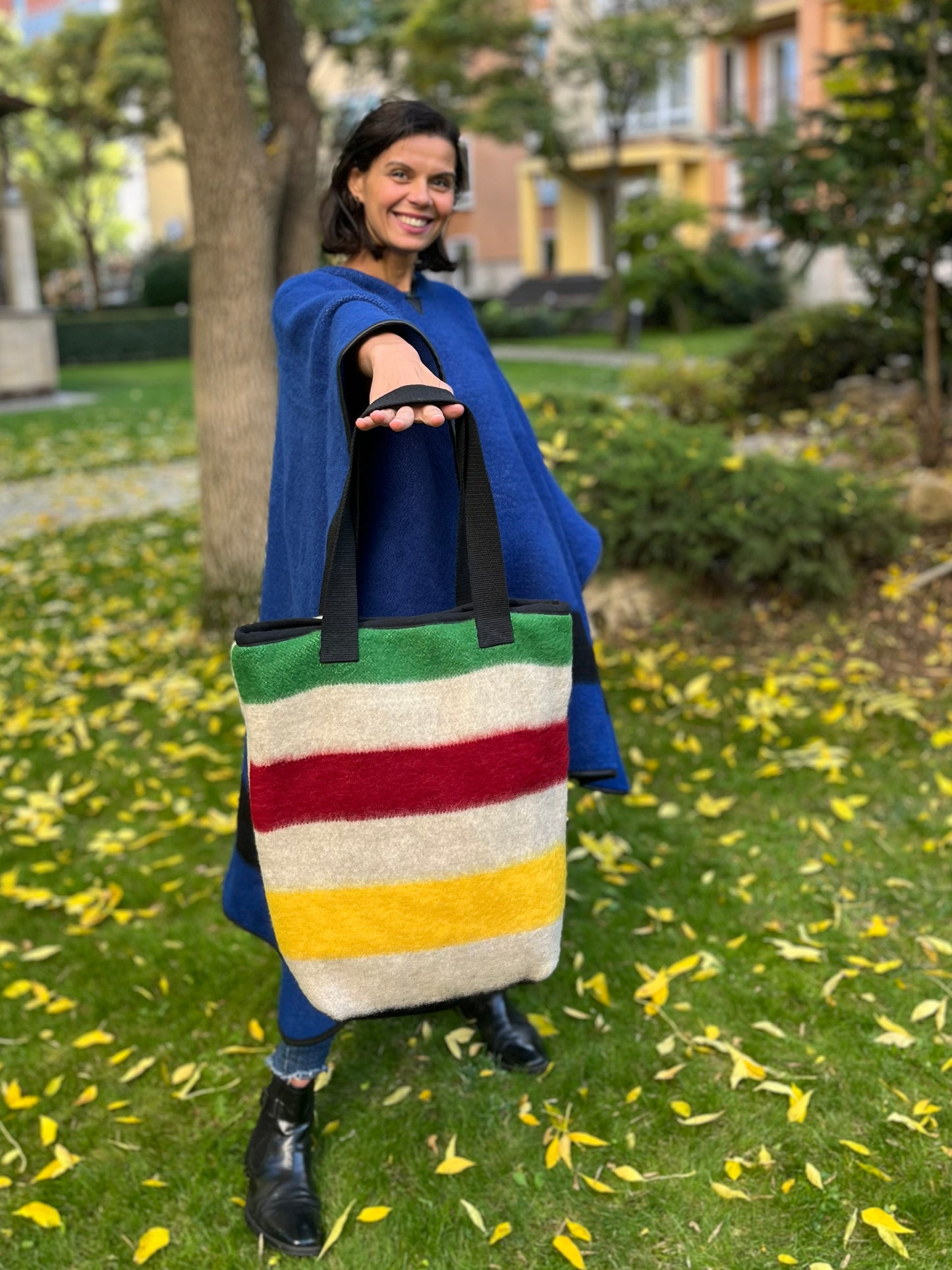 Woman holding a native-american style striped bag in an outdoor setting with trees and buildings in the background.