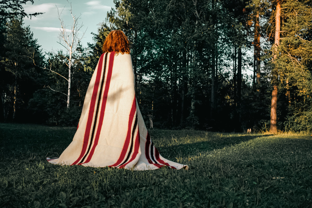 Woman standing backwards wrapped in pure wool throw blanket in warm ivory with multicolor woven stripes