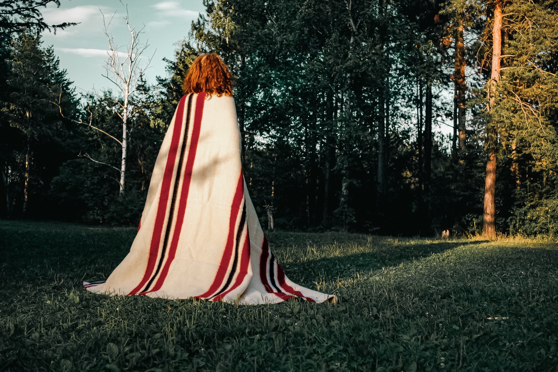 Woman standing backwards wrapped in a cream wool Heritage Blanket, handmade from pure sheep wool.
