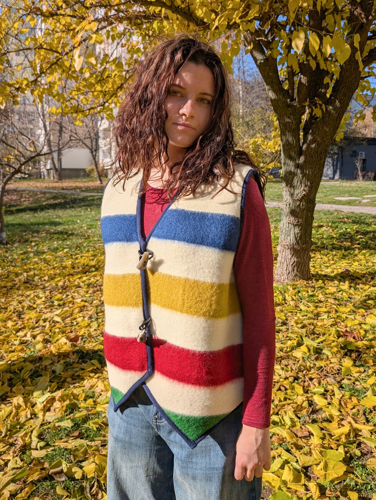 A young woman looking stylish upcycled blanket vest with statement multicolor stripes and big horn toggles. 