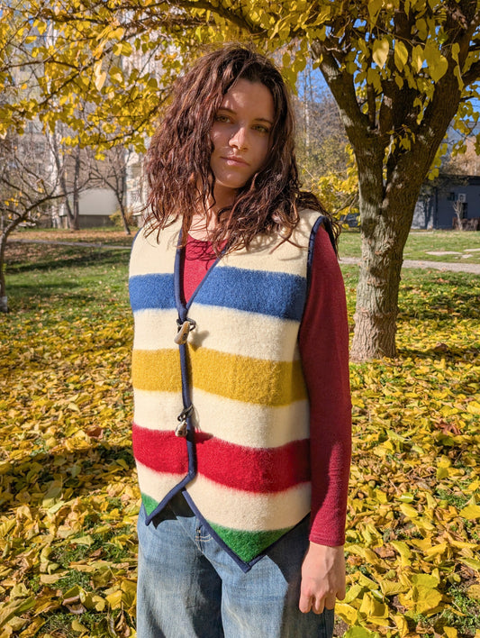 A young woman looking stylish upcycled blanket vest with statement multicolor stripes and big horn toggles. 