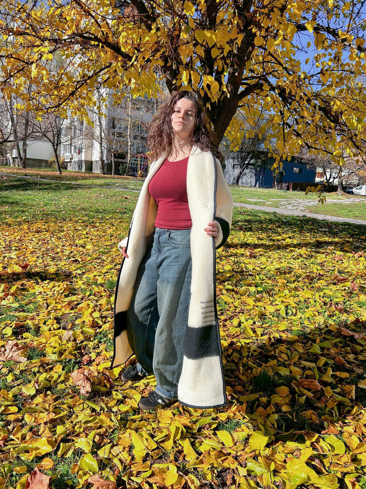 Young woman wearing a heavy wool coat tailored from upcycled natural wool blanket. The coat is cream color with black stripes. Statement Wool Coat.