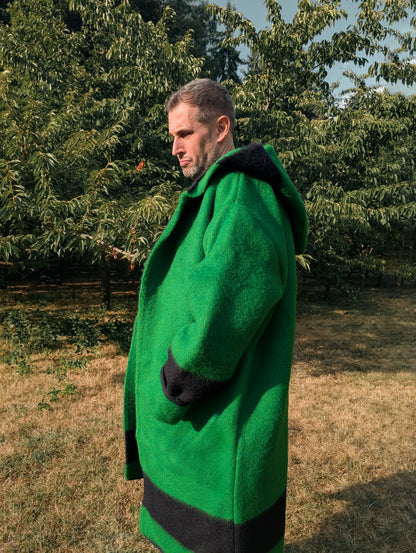Person wearing a loose hooded robe coat made from green blanket with black stripes of natural poor wool.