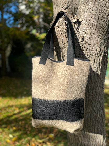 Gray handmade tote bag with black straps  and a signature black stripe, hanging on a tree in an outdoor setting
