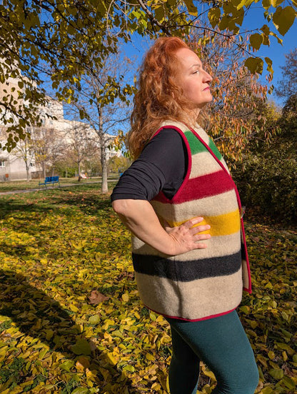 Woman wearing a cool sleeveless wool jacket with colorful stripes and red edging. The model has a shawl collar.