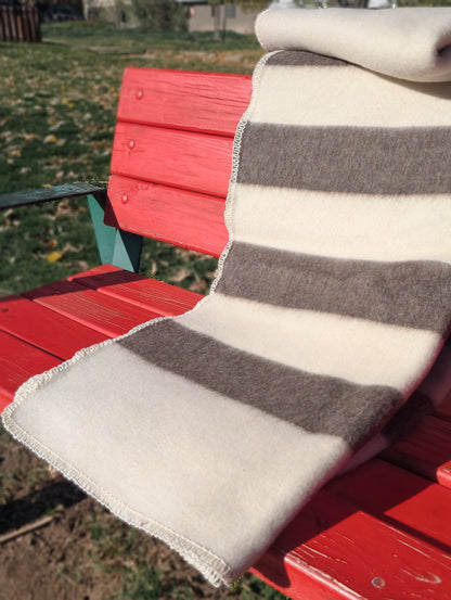 Luxurious Minimalistic Striped wool blanket with natural ivory and brown tones, exposed on a red bench outdoors