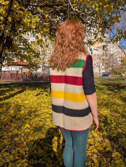 Person wearing a unisex multistripe wool blanket vest, standing in a park with autumn leaves.