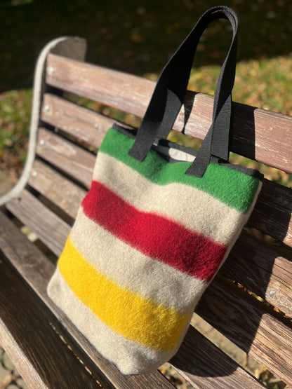 North american heritage style tote bag with stripes ina green, red, and yellow colors on a wooden bench.