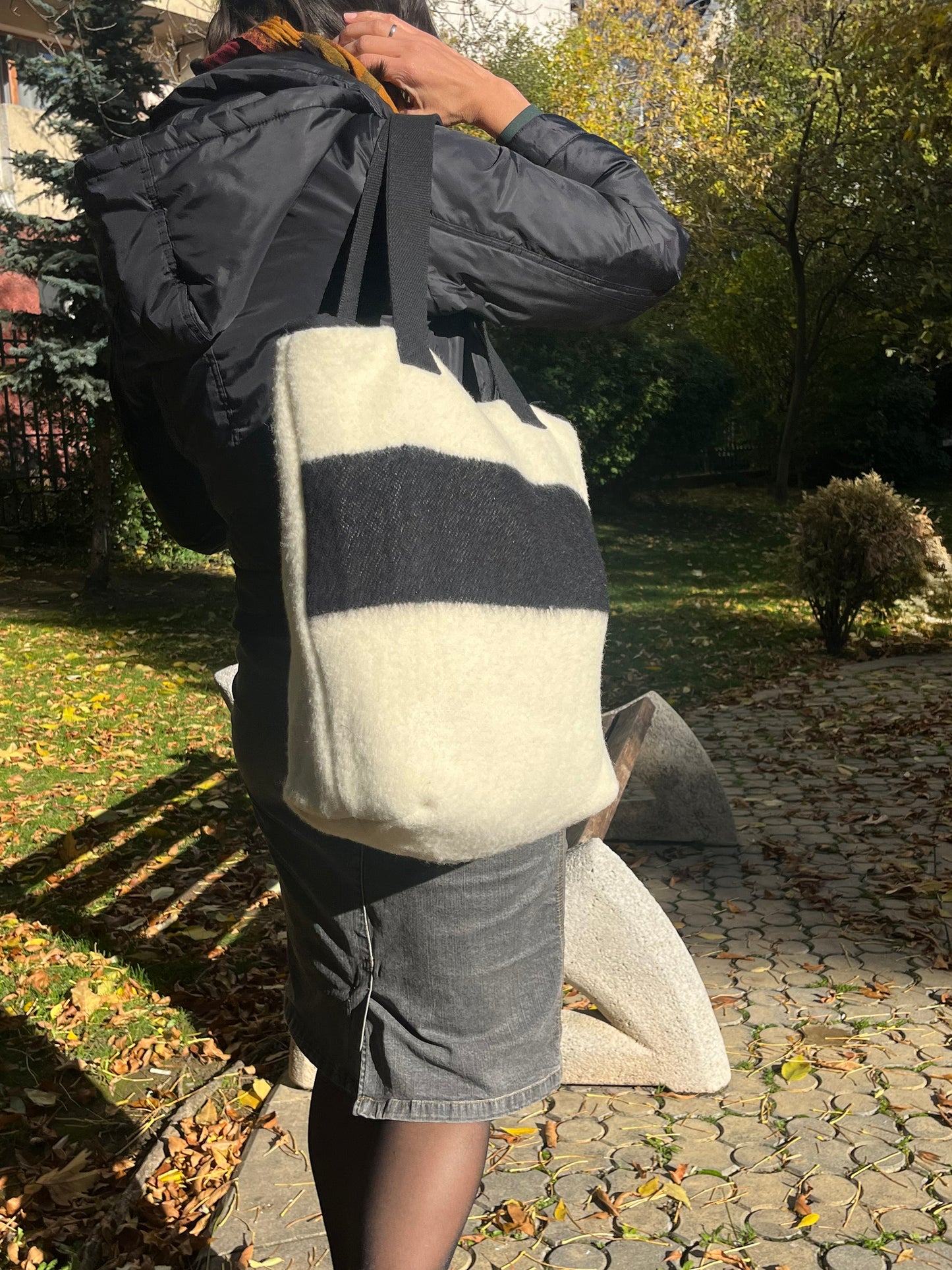 Woman wearing a stylish handcrafted modern wool bag in ecru with black stripe, made from repurposed traditional blanket.