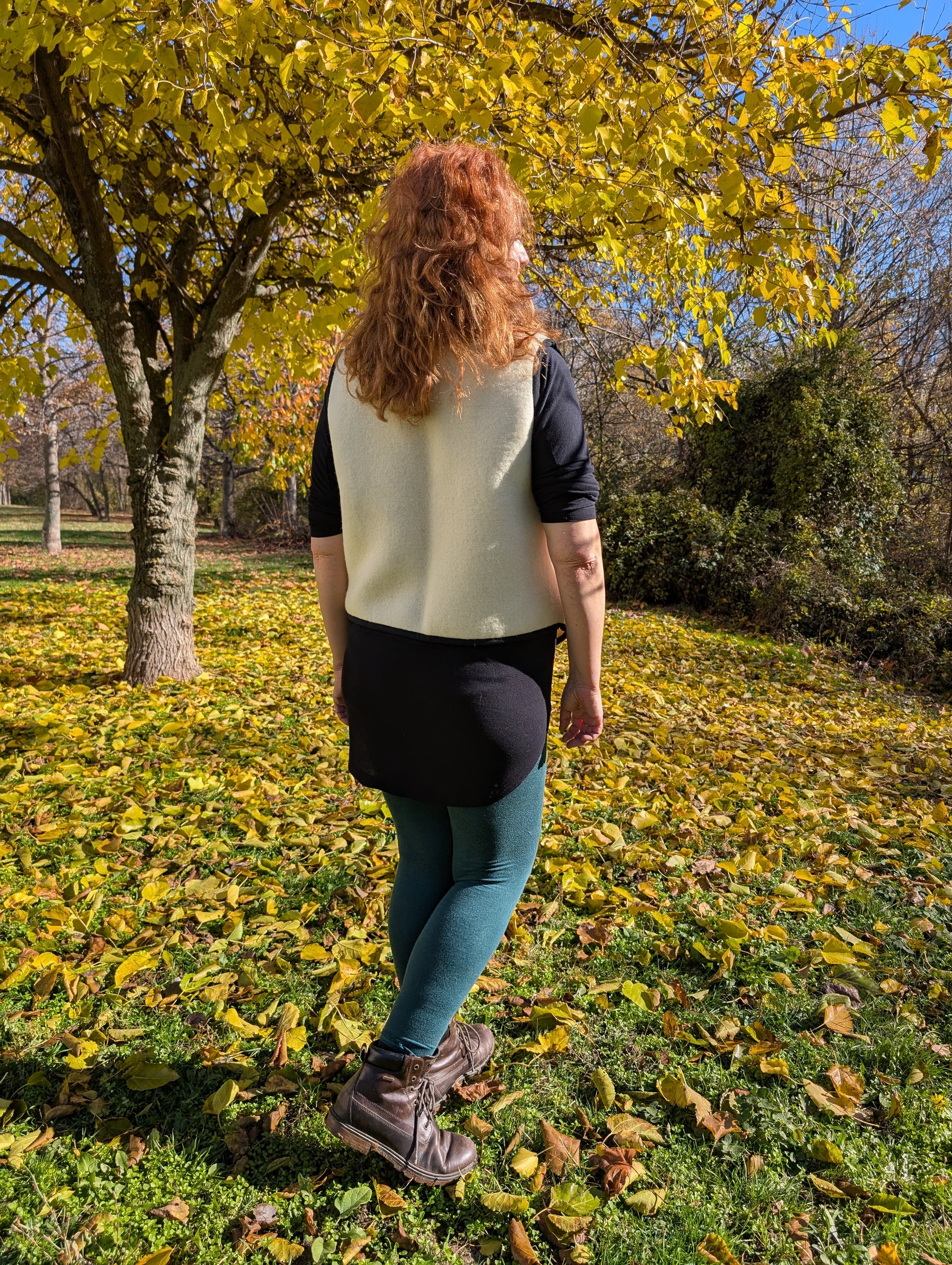 Woman standing with her back, wearing a made-to-order wool blanket vest, upcycled from a new ivory wool blanket with a black stripe in front.