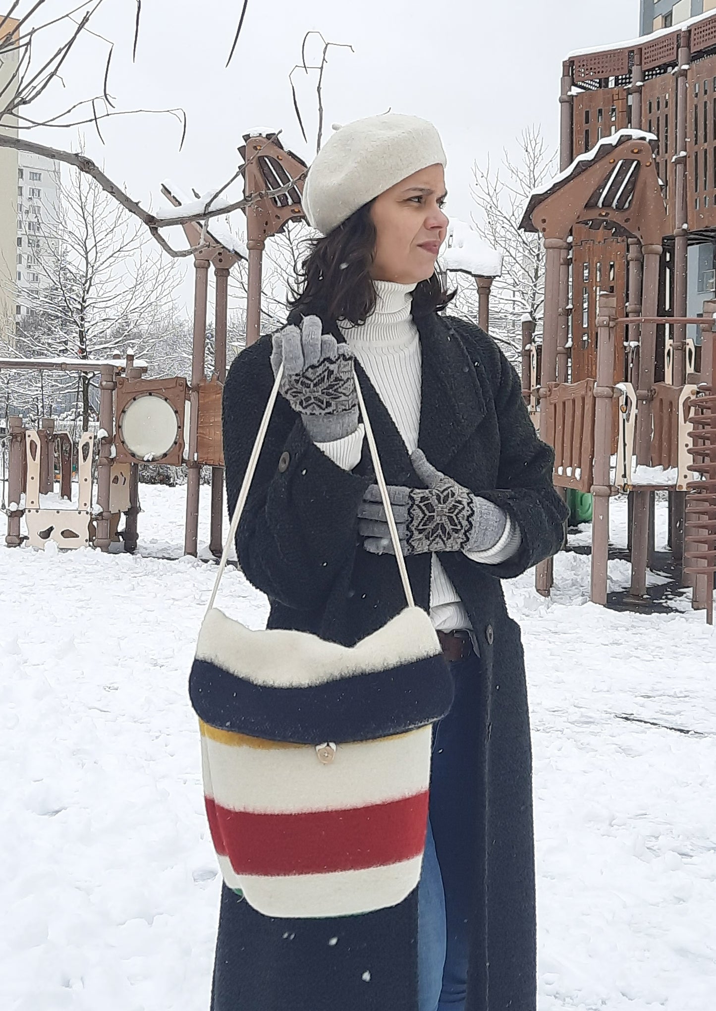 Woman holding a colorful striped bag in a snowy playground.