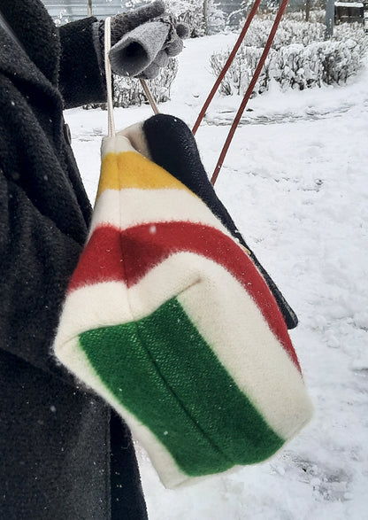 Colorful striped tote bag with rope straps, held by a person in a snowy outdoor setting. The bag is made from pure wool blanket.