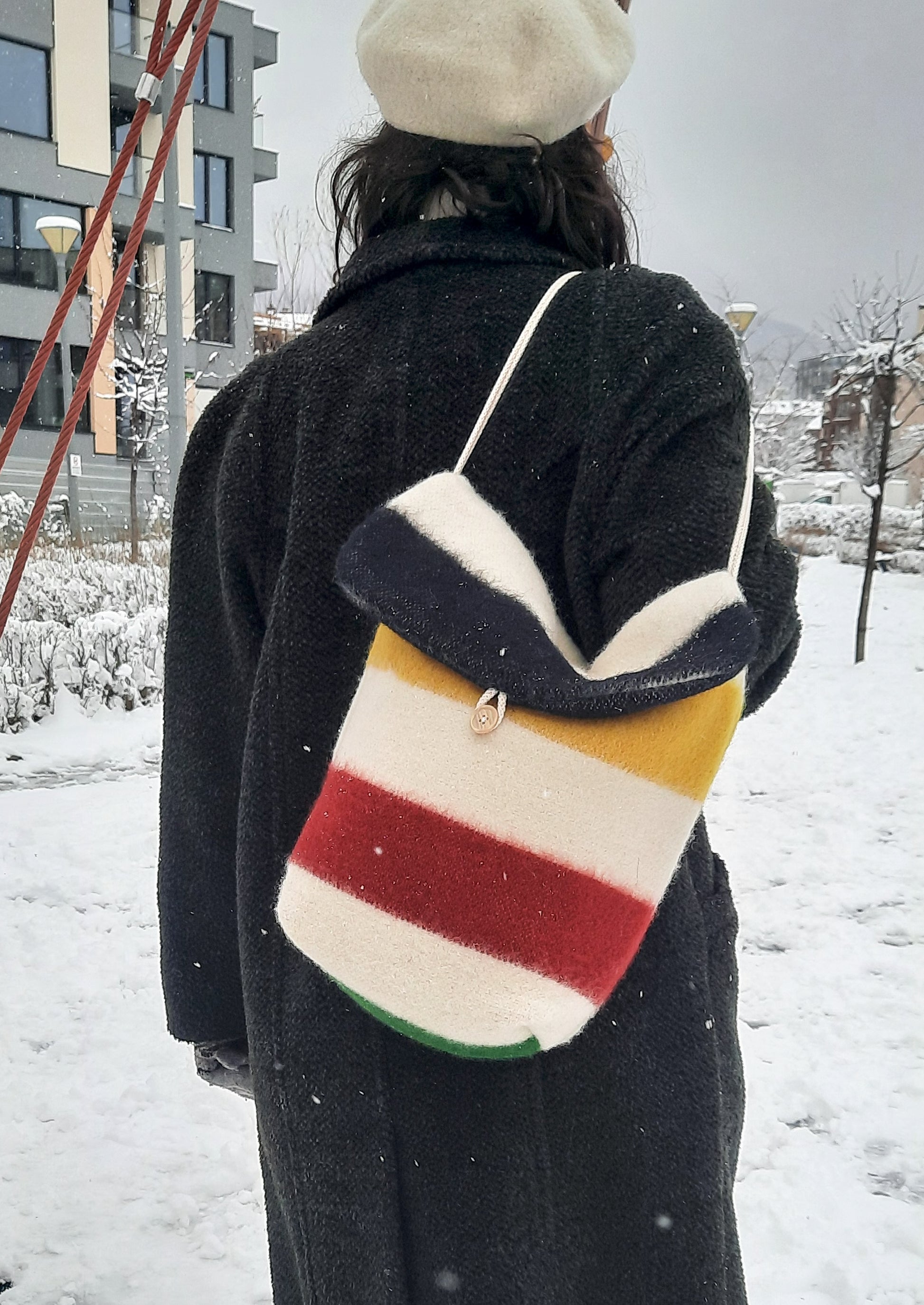 Woman wearing a stylish compact shoulder bag with colorful stripes and rope handles, made of traditional wool blanket leftovers.