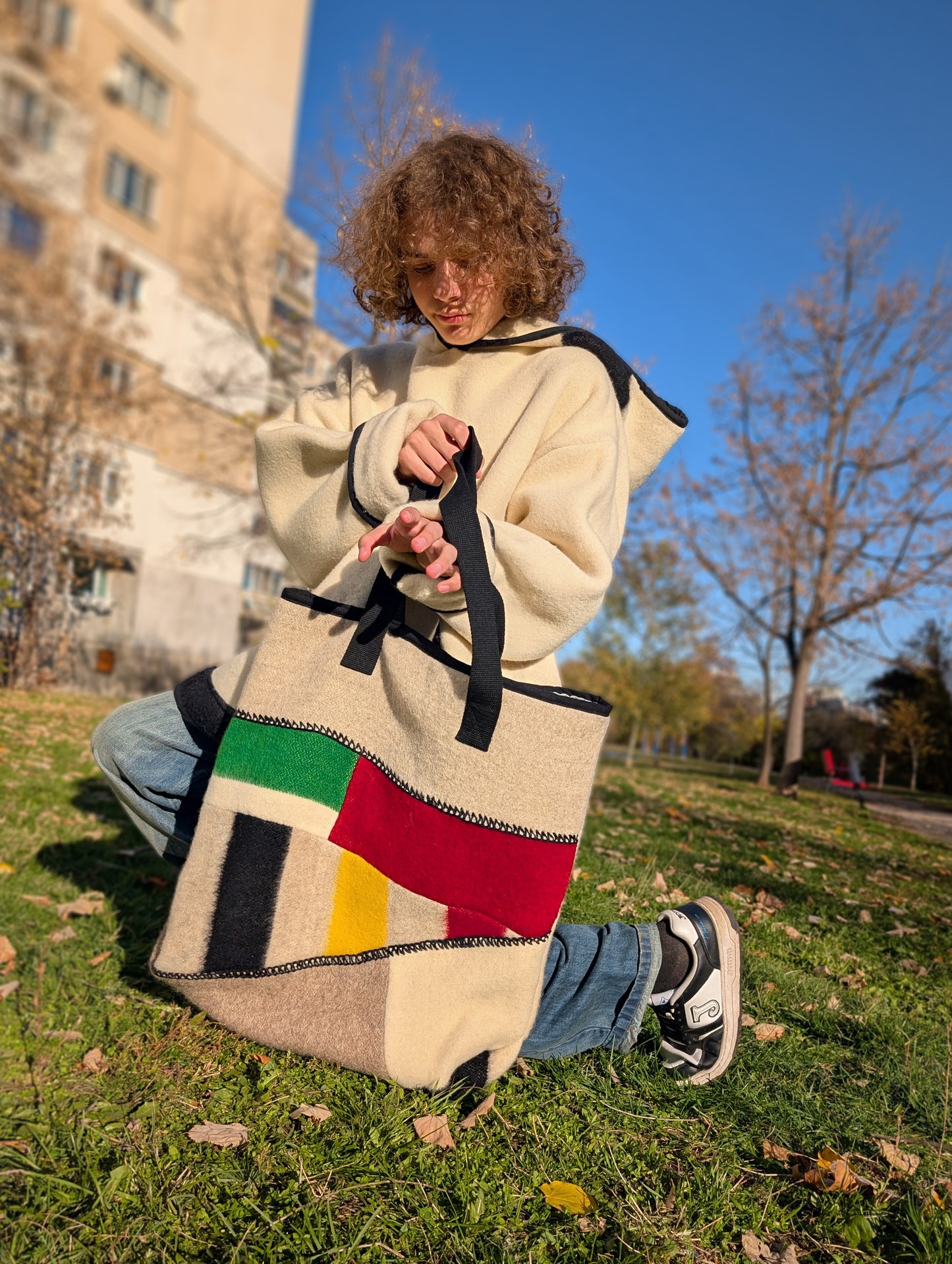 Young man holding a colorful tote bag with geometric patterns, patched from wool blanket leftovers.