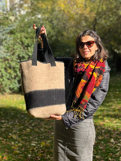 Woman holding a modern woolen handbag with minimalistic design in pastel brown to gray base with a black stripe.