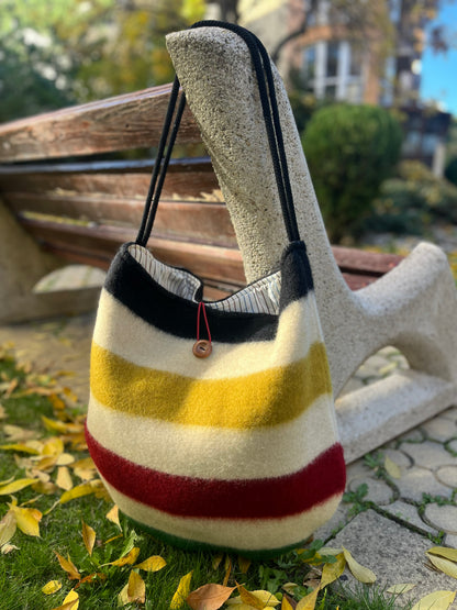 Modern boho striped bag with a toggle button closure hanging on a stone bench outdoors