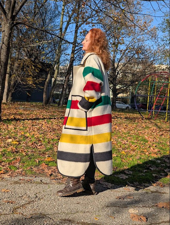 Woman wearing a colorful striped wraped coat in an outdoor setting with trees and playground equipment.