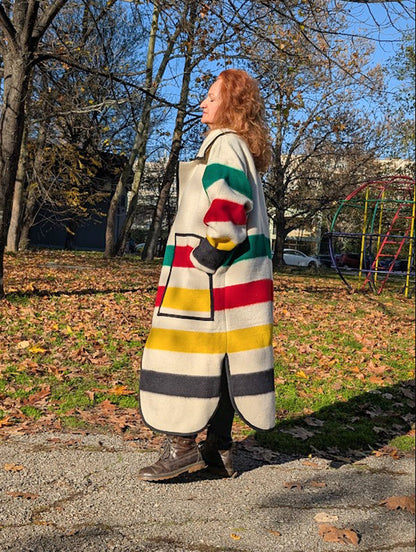 Woman wearing a colorful striped wraped coat in an outdoor setting with trees and playground equipment.