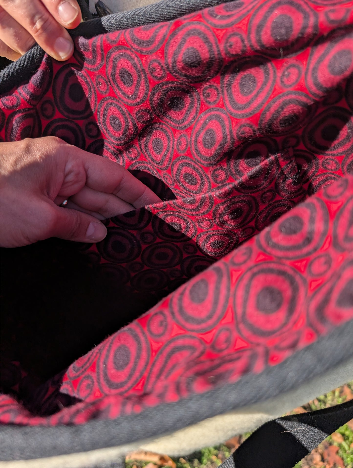 Close-up of a red and black patterned cotton bag interior lining with a hand showing the bag's inside pocket.