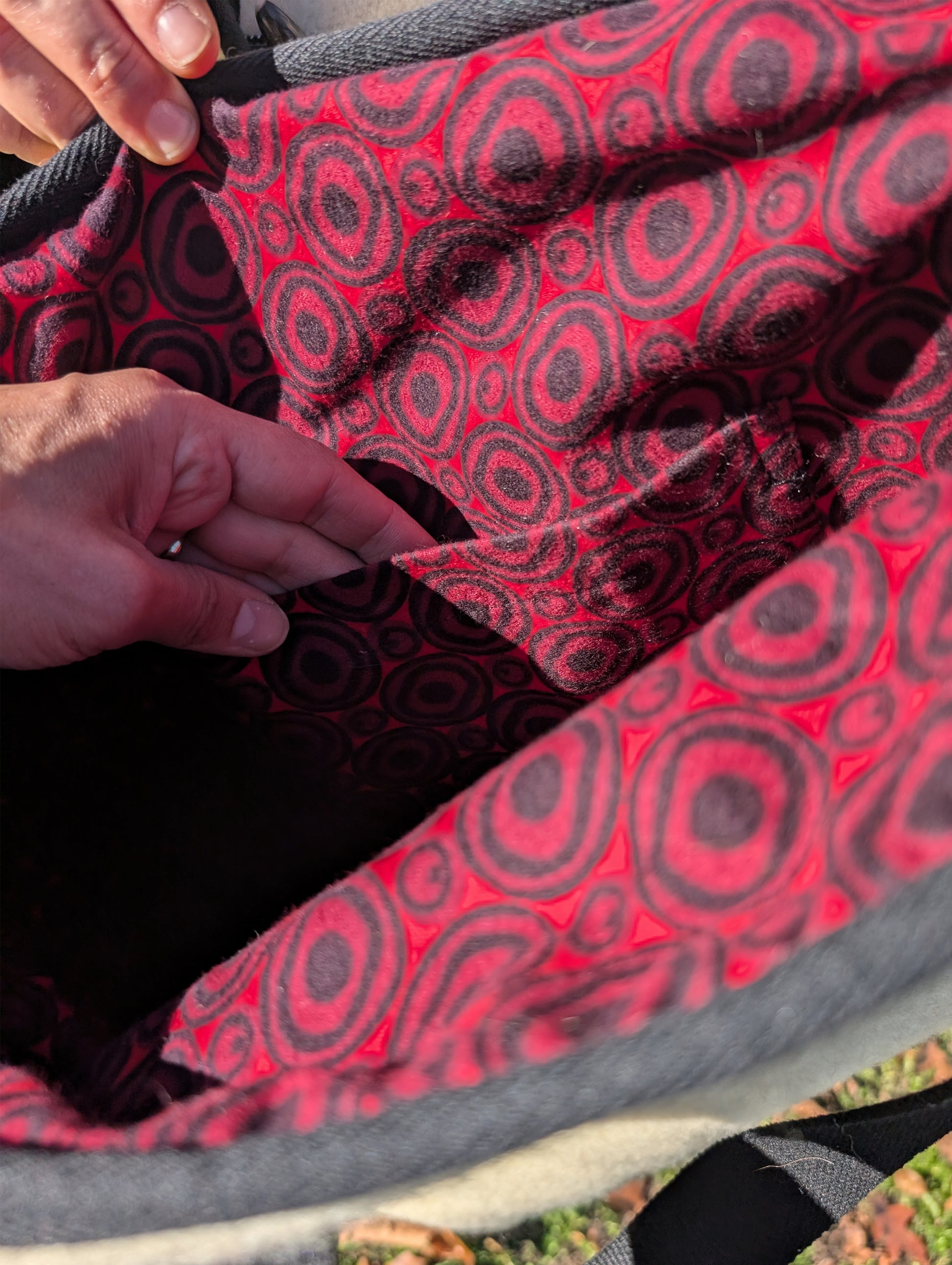 Close-up of a red and black patterned cotton bag interior lining with a hand showing the bag's inside pocket.